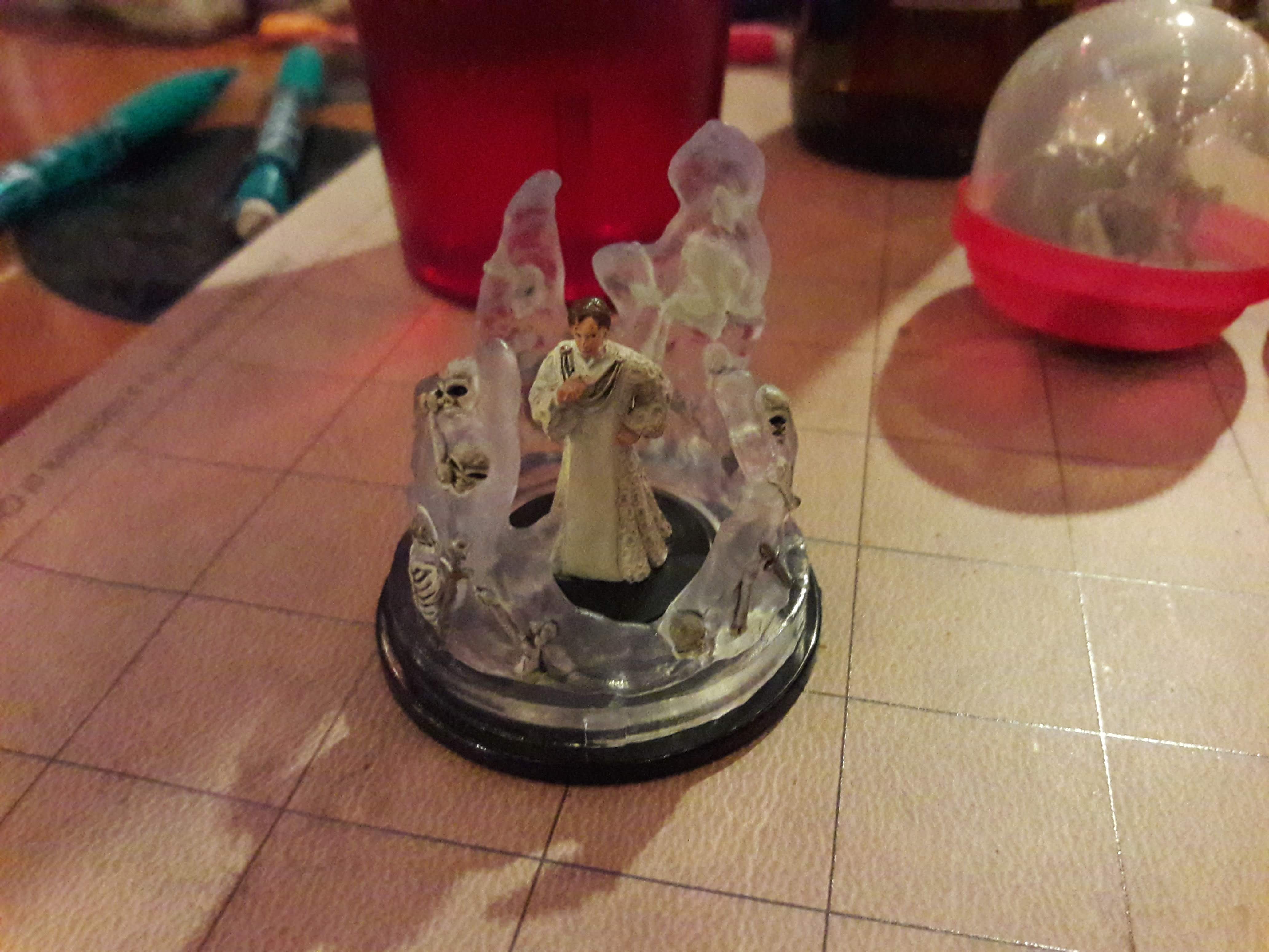 A close up shot of a miniature figure of Mon Mothma surrounded by clear walls. The walls contain parts of skeletons and discarded weapons.