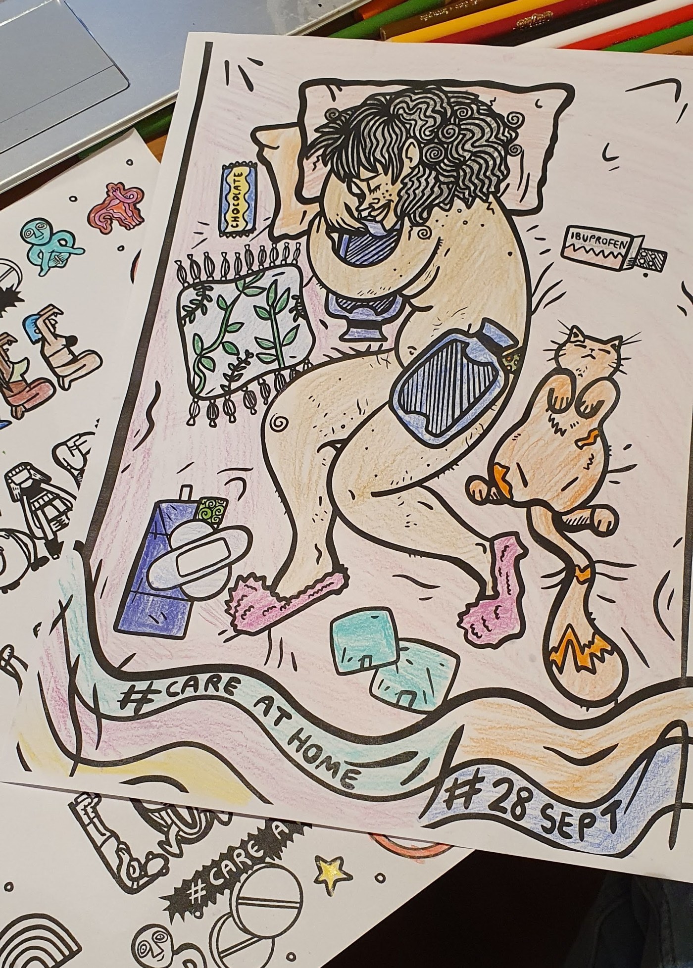 two colouring pages overlapping each other. A laptop keyboard and colouring pencils are in the background. In the top picture, someone is cuddling a water bottle while lying on a bed and surrounded by chocolate, pills, pads and a cat.
